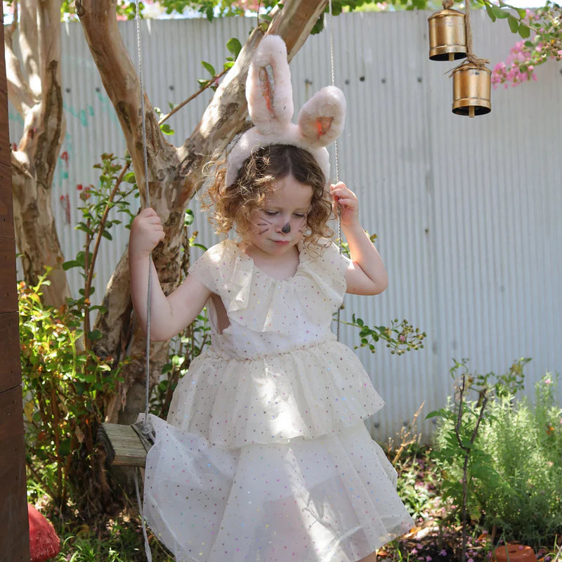 A child wearing the Fluffle Bunny Ear Headband in pink by Olli Ella, playing on a swing in a garden, highlighting the headband's charming look in a playful setting.