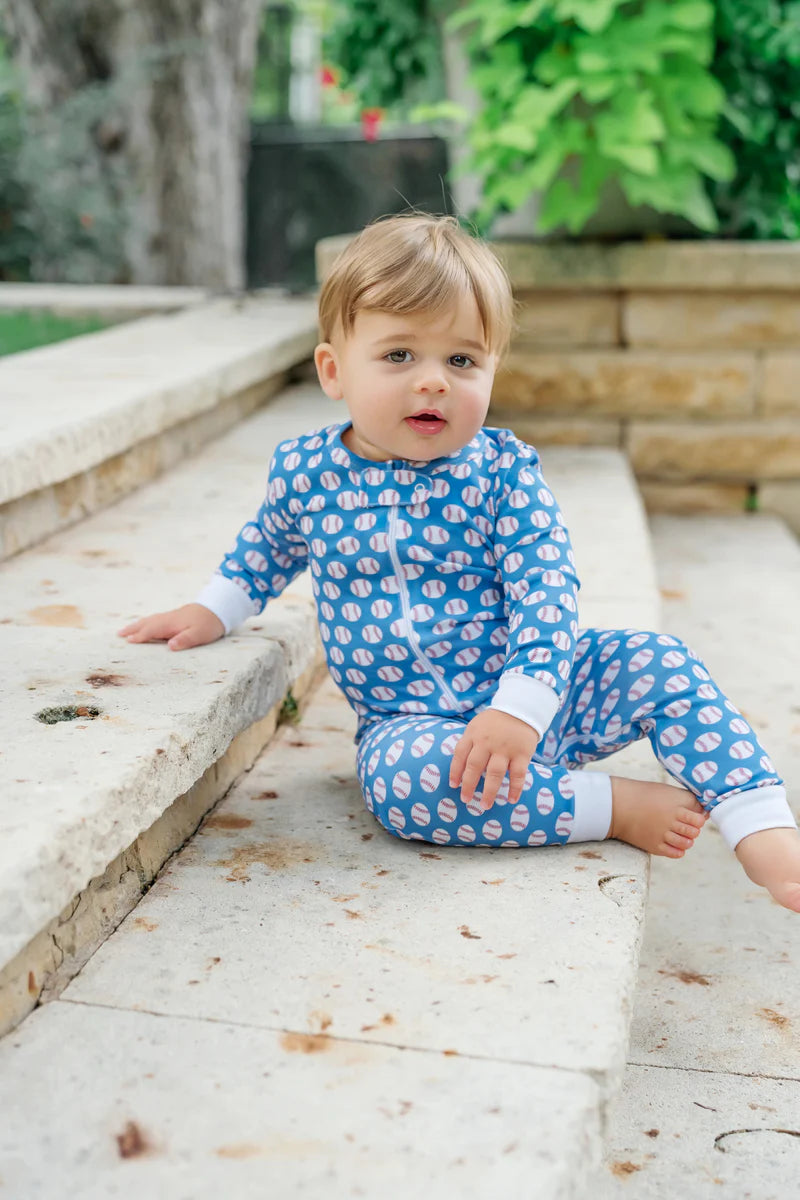 A cute baby wearing the Parker Zipper Pajama Baseball Grand Slam by Lila and Hayes, sitting on outdoor steps, highlighting the pajama's comfort and style.