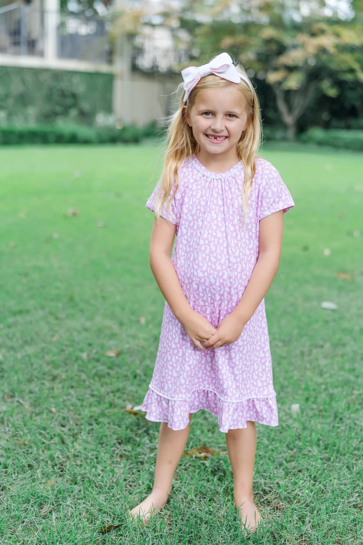 A happy child outdoors, wearing the Lila and Hayes Camden Dress - Short Sleeve Pima Cotton Children Dress, with a flutter ruffle hem in Easter Time Pink.