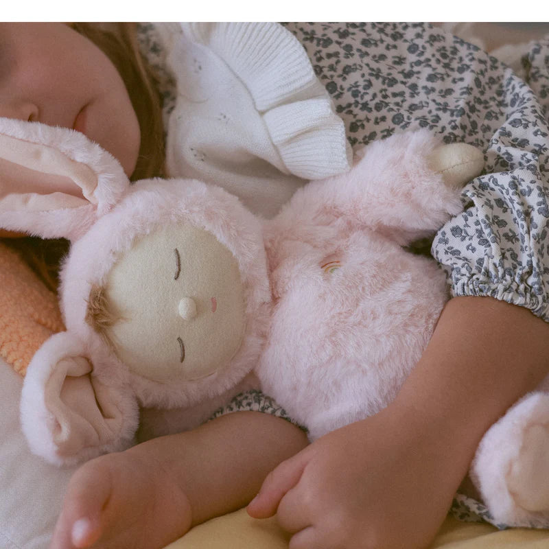 A child peacefully sleeping with the Lullaby Cozy Dinkums Bunny Moppet by Olli Ella, pink plush bunny draped in their arms.