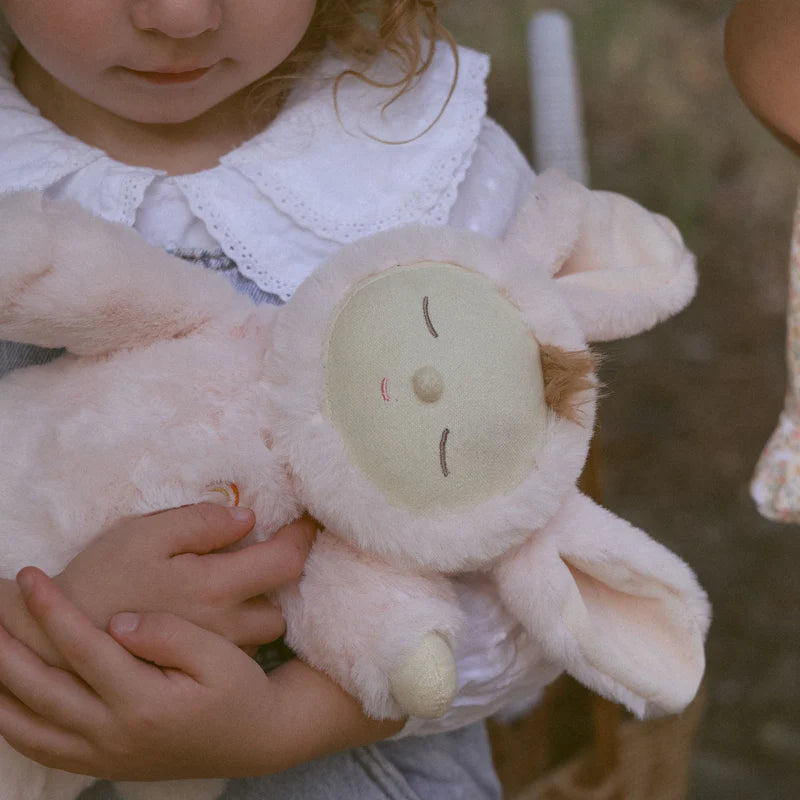 A young child gently cradling the Lullaby Cozy Dinkums Bunny Moppet by Olli Ella, showcasing the adorable pink plush toy.