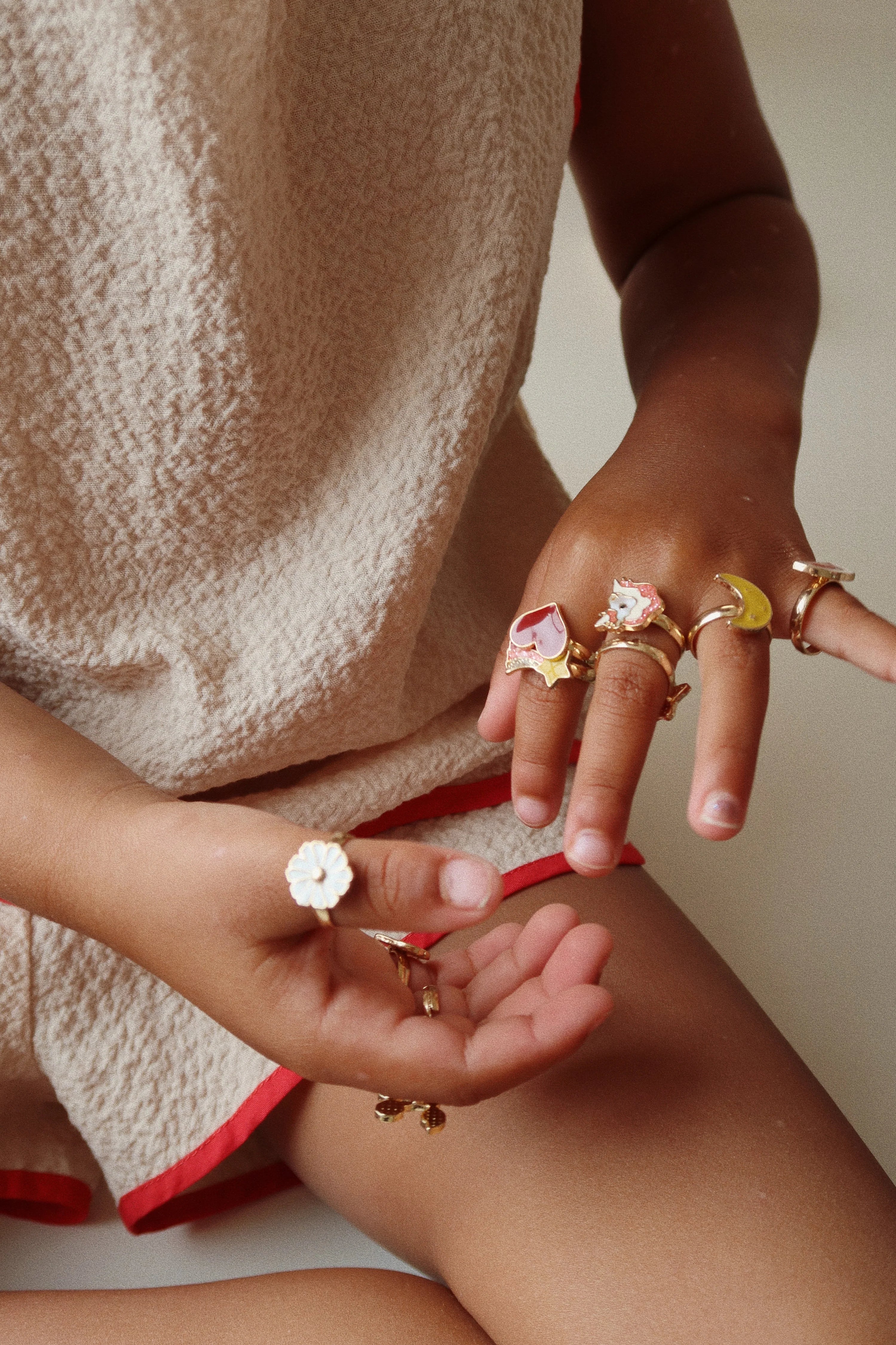 A close-up of a child's hands wearing multiple rings from the 12 Pack Ring Set from Konges Slojd, highlighting the fun designs and colors.