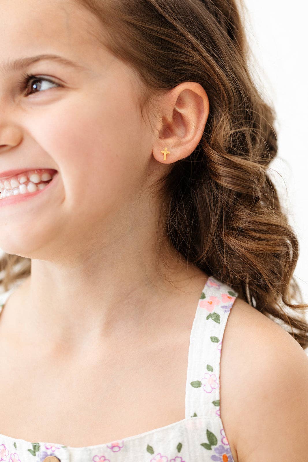 A smiling young girl wearing Cross Earrings from Pip Pop Post, showcasing their cute and comfortable design.